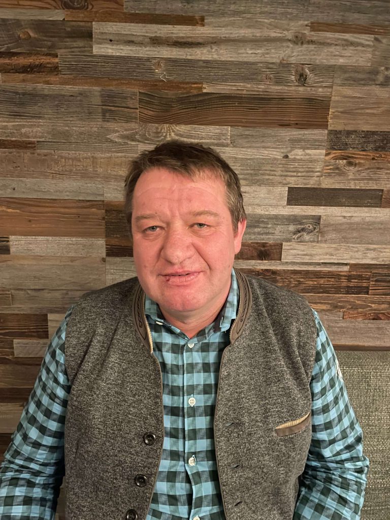 Rupert Steiner, Zimmerer-Hilfsarbeiter bei Holzbau Gläser seit 2020, vor Holzpaneelen.