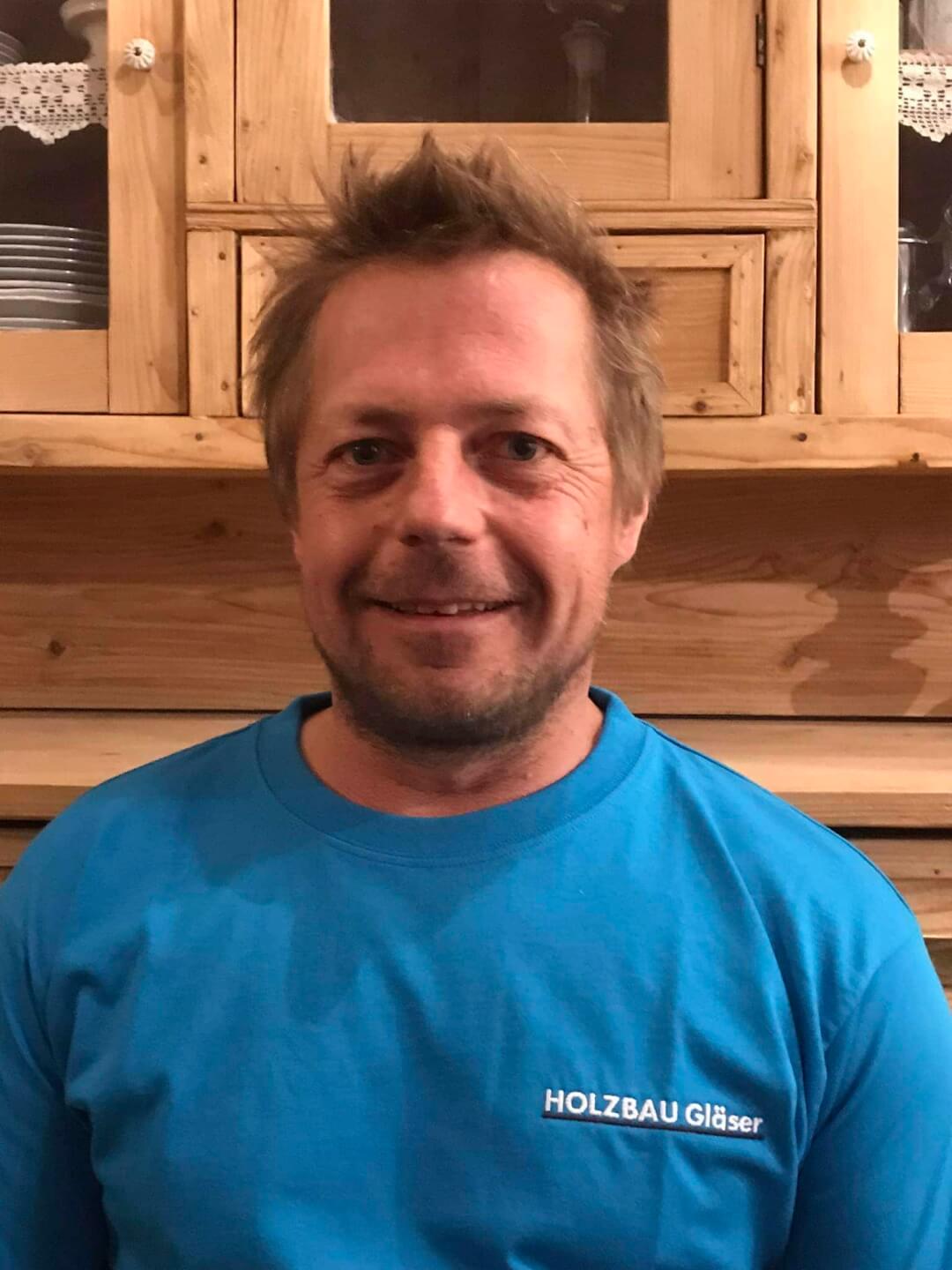 Thomas Gläser in Arbeitskleidung, Hintergrund aus Holz mit Regalen. Holzbau-Expertise.